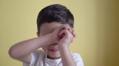 Sevimli çocuk gülümsüyor ve yüzünü renk arka planında örtüyor.