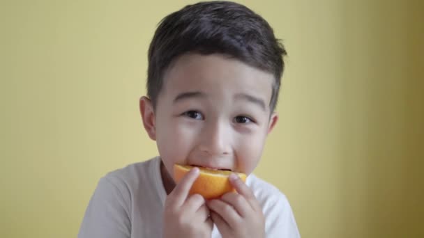 Yakışıklı Asyalı çocuk arka planda bir parça turuncu yiyor. — Stok video