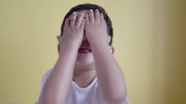 Sevimli çocuk gülümsüyor ve yüzünü renk arka planında örtüyor..