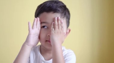 Sevimli çocuk gülümsüyor ve yüzünü renk arka planında örtüyor.. 