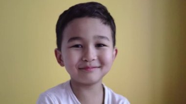 Sevimli çocuk gülümsüyor ve yüzünü renk arka planında örtüyor.