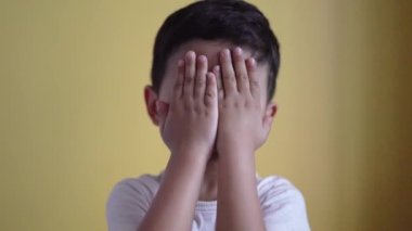 Sevimli çocuk gülümsüyor ve yüzünü renk arka planında örtüyor.