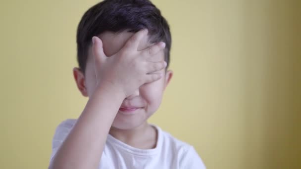 귀여운 소년이 웃으면서 컬러 배경으로 얼굴을 가리고 있다. 파피알 름 — 비디오