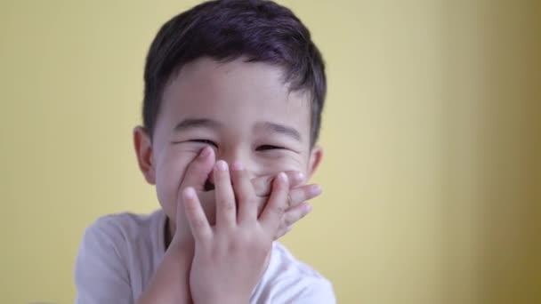 Lindo chico risa y cubrir su boca en color de fondo — Vídeos de Stock