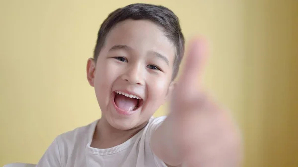 Cheerful preschooler smiling and showing thumbs up on colour background — Stock Photo, Image