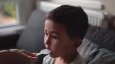A child drinks syrup from a spoon given to him by his mother. High quality 4k footage