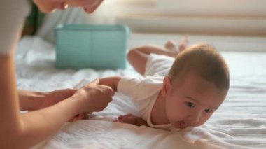 Mother helps to turn over to her baby boy on big bed. Babys turn over exercises . High quality 4k footage