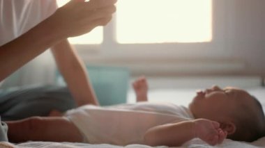 Mother distracts a child lying on the bed with a toy. High quality 4k footage