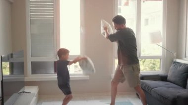 Young Father and little son enjoy pillow fighting sit on sofa at home. High quality 4k footage
