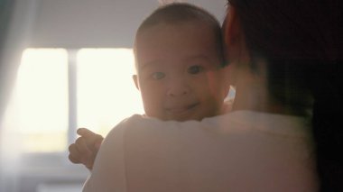 Side view of Mother holds her baby. Close up view of cute baby looking at camera. High quality 4k footage