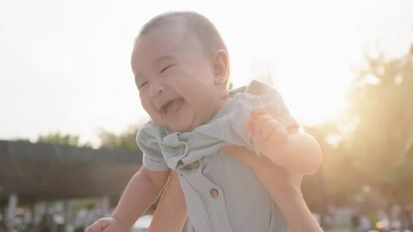 Happy mom throws up a baby. Cute small laughing baby. Happy family in park. Portrait in front of the sunset. High quality 4k footage