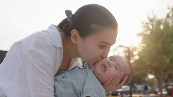 Happy mom holding and kissing baby. Happy family in park. High quality 4k footage