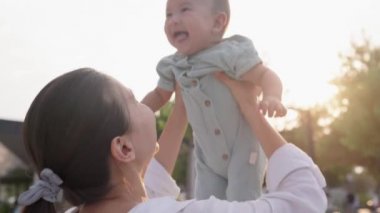 Happy mom throws up a baby. Cute small laughing baby. Happy family in park. Portrait in front of the sunset. High quality 4k footage
