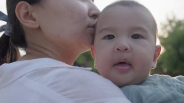 Close up view of Happy mom holding and kissing baby. Happy family in park. High quality 4k footage