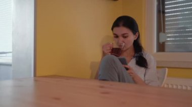 Woman drinks a tea and watching a mobile phone. High quality 4k footage