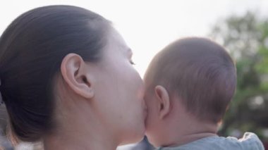 Close up view of Happy mom holding and kissing baby. Happy family in park. High quality 4k footage