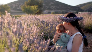Beautiful woman with baby on lavender fields at sunset. Wreath of lavender. High quality 4k footage