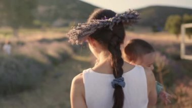 Rear view of Beautiful woman with baby on lavender fields at sunset. Wreath of lavender. High quality 4k footage