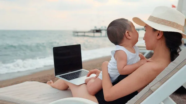 Mother with baby working on laptop near the sea. Remote work concept. work on vacation. 4 k. High quality 4k footage