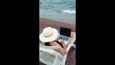 Rear view of freelancer woman working on laptop near the sea. Remote work concept. work on vacation. High quality 4k footage