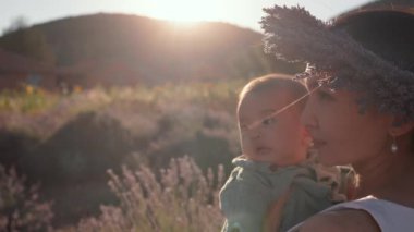 Beautiful woman with baby on lavender fields at sunset. Wreath of lavender. High quality 4k footage