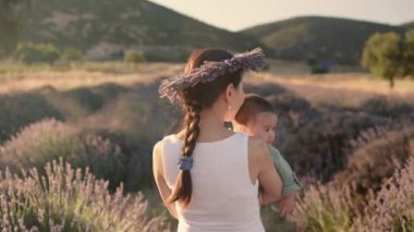 Rear view of Beautiful woman with baby on lavender fields at sunset. Wreath of lavender. High quality 4k footage