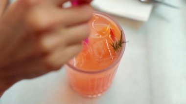 Female hand stir an orange lemonade with ice in transparent glass. High quality 4k footage