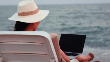 Freelancer woman working on laptop near the sea. Remote work concept. work on vacation. High quality 4k footage