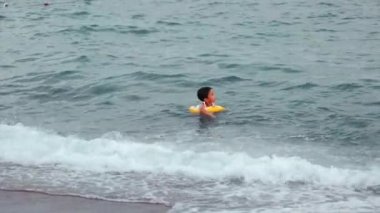 Happy Little child with swimming circle swims on the sea. Boy has fun on waves. High quality 4k footage