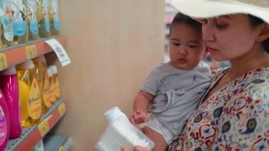Young modern single mother choosing baby cream in supermarket. High quality 4k footage