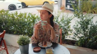 Rear view of young woman in hat drinking a coffee with dessert. High quality 4k footage