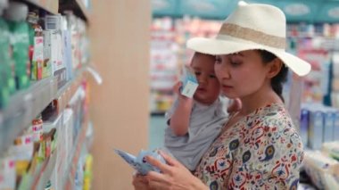 Young modern single mother choosing baby cream in supermarket. High quality 4k footage