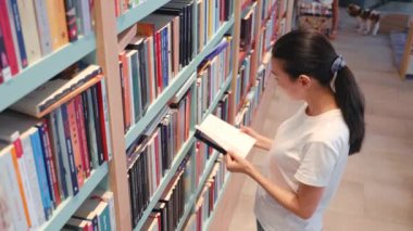Top view of Young woman leafing through a book in library. University. Public library. office bookshelves. Book store. High quality 4k footage