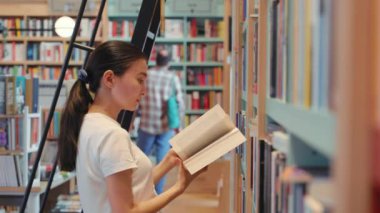 Young woman leafing through a book in library. University. Public library. office bookshelves . High quality 4k footage