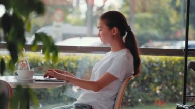Young freelancer woman typing on laptop sitting at cafe. Remote work concept. High quality 4k footage