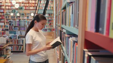 Young woman leafing through a book in library. University. Public library. office bookshelves . High quality 4k footage