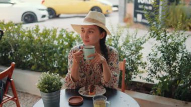 Rear view of young woman in hat drinking a coffee with dessert. High quality 4k footage