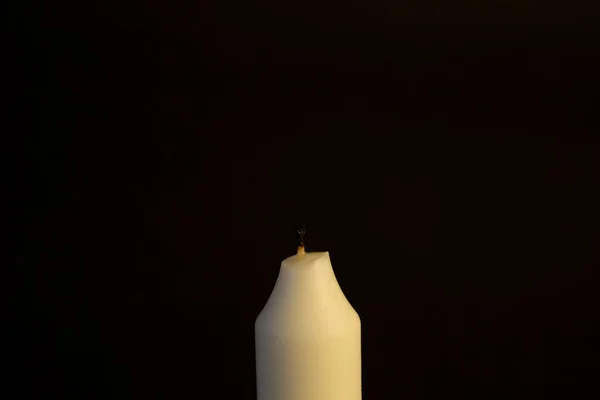 a white candle on a black background, an extinguished candle.