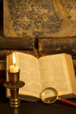 Masadaki eski kitaplar, mum ışığında okumak, büyüteç.