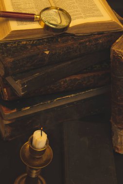 Masadaki eski kitaplar, mum ışığında okumak, büyüteç.