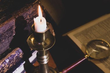 Masadaki eski kitaplar, mum ışığında okumak, büyüteç.