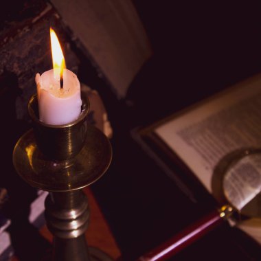 Masadaki eski kitaplar, mum ışığında okumak, büyüteç.