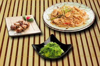 Asya yemeklerinin tam menüsü. Bambu masa örtüsü üzerinde sunulan üç yemek. yatay çerçeve