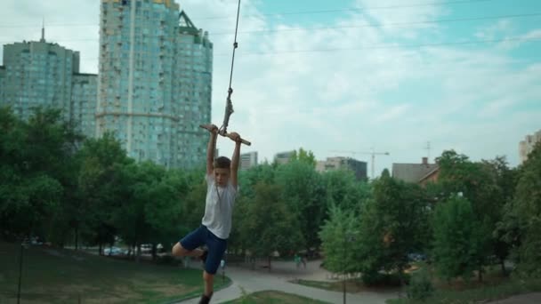 Garoto ativo balançar no bungee caseiro na árvore ou se divertir no parque da cidade ao ar livre — Vídeo de Stock