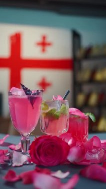 Pembe kokteyl ve limonata bardakta ve masaya düşen gül yaprakları.