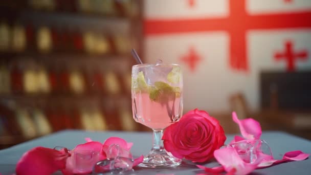 Cocktail rose ou boisson de limonade en verre et pétales de rose tombant sur la table — Video