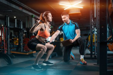 Genç bayan spor yapıyor ve spor salonunda kişisel antrenörle halter çalışıyor.
