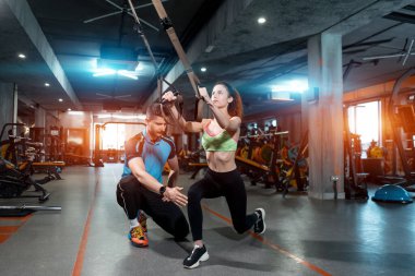 Genç bayan spor yapıyor ve spor salonunda Trx ve kişisel antrenörle antrenman yapıyor.