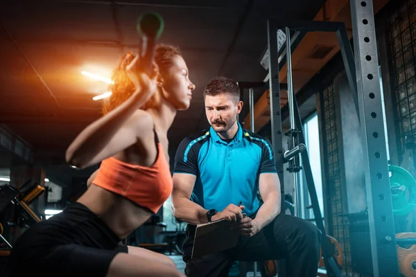 Jonge vrouwelijke training en het trainen van lange halter squat in de sportschool met personal trainer — Stockfoto