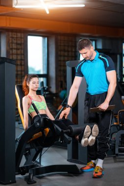 Spor salonunda antrenörle bacak açma egzersizi yapan genç bir kadın.